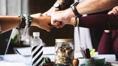 five people fist bumping over desk supplies